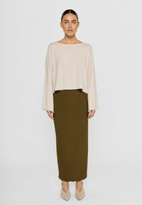 Lysbeige ribbet cropped top med brede ærmer, parret med en lang olivengrøn ribbet nederdel. Beige perforerede høje hæle.
