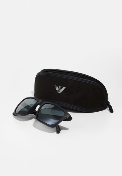 Ochelari de soare negri cu lentile întunecate, având un design pătrat. Însoțiți de un toc negru cu fermoar, având un logo pe față.