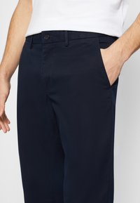 Marinblå byxor av ett slätt tyg med rak front, sidofickor och en enkel knappstängning i midjan.