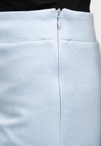 Jupe bleu clair texturée avec une fermeture éclair à l'arrière et deux poches horizontales. Le tissu présente une finition subtilement imprimée.