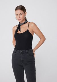 Zwarte geribbelde tanktop met dunne bandjes, gecombineerd met high-waisted donkere jeans. Heeft een zwart-wit patroonsjaal die om de nek is geknoopt.