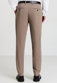 Pantaloni eleganti beige con una texture liscia, taglio dritto, passanti per cintura, due tasche posteriori con bottoni, abbinati a scarpe nere.