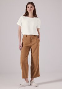 T-shirt bianco a maniche corte abbinato a pantaloni larghi beige a vita alta. Le scarpe sono chiare e dal design semplice.