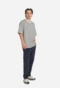 Striped T-shirt in cream and navy, relaxed fit, short sleeves, featuring a front pocket; paired with dark pants and sneakers.