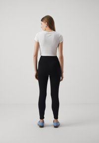 White ribbed crop top with short sleeves, paired with high-waisted black leggings. Model wears light blue shoes, facing away from the camera.