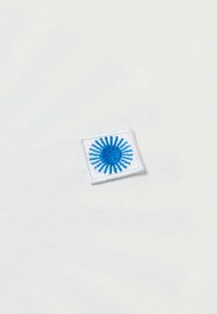Witte stoffen t-shirt met een vierkante geborduurde patch met een blauw zonnestraalontwerp, gestikt aan de linkerzijde.