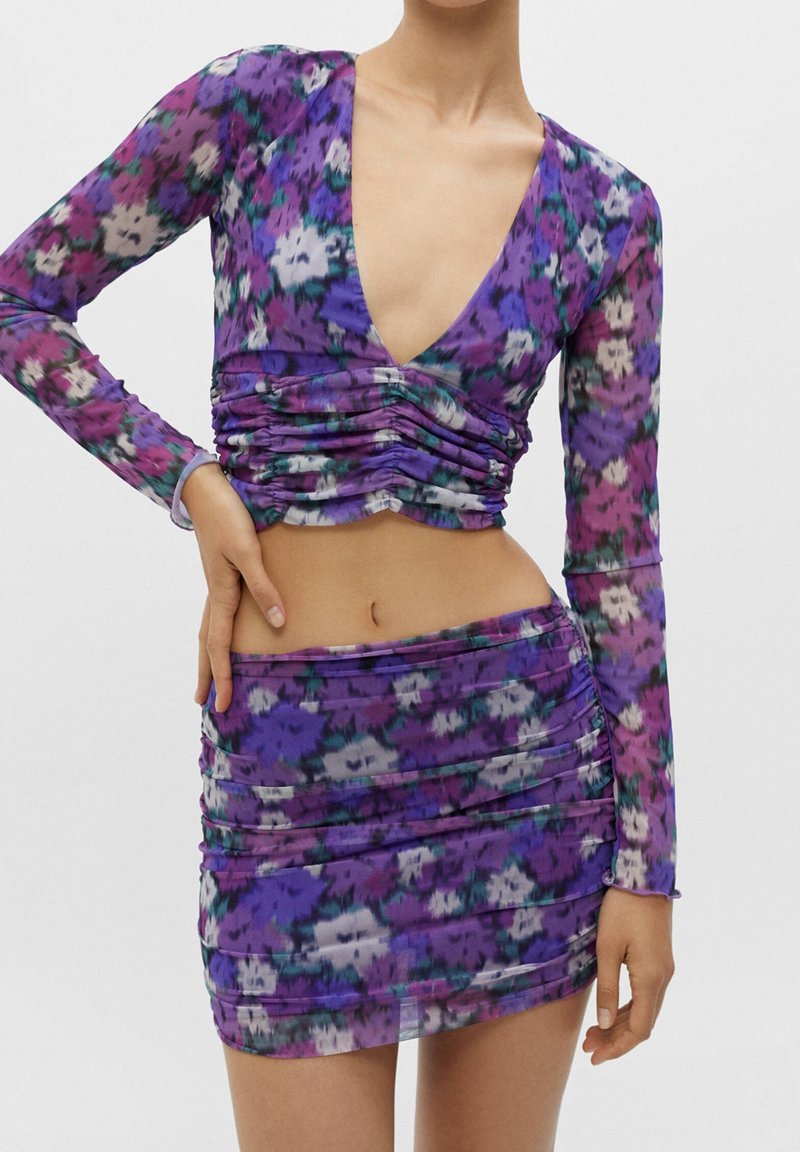 Blomster-mønstret crop top og mini nederdel sæt i lilla, med lange ærmer, dyb V-hals og samlede detaljer i blødt, gennemsigtigt stof.