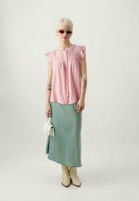 Helles pinkes Hemdbluse mit Rüschensämlen, kombiniert mit einem mintgrünen Satin-Midikleid. Die Accessoires umfassen eine weiße Handtasche und Sonnenbrille.