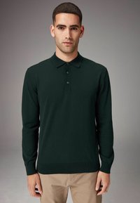 Pólo de manga larga de color verde oscuro en material de punto, con cuello, tapeta de tres botones y puños acanalados. Textura suave, diseño ajustado.