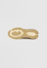 Shoe sole in cream and light brown rubber, featuring curved traction patterns and a circular cutout for flexibility and grip.