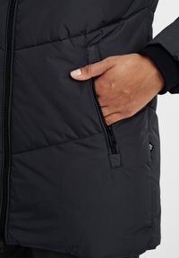 Čierna prešívaná bunda s bočnou vreckom na zips, hladkou textúrou a tesným strihom so subtílnymi švovými detailmi.