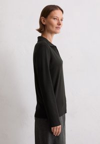 Czarna longsleeve polo z gładkiego materiału, z klasycznym kołnierzykiem i prostym krojem, zestawiona z szarymi teksturowanymi spodniami.