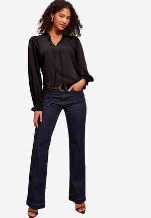 Black, long-sleeve blouse with gathered cuffs and a V-neck design, paired with dark blue flared jeans featuring a straight cut and subtle stitching.