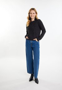 Grauer langärmliger Pullover mit entspanntem Design, kombiniert mit hoch taillierten blauen weiten Jeans und schwarzen spitzen Ankle Boots.