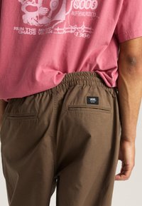 Pink graphic t-shirt with a round neck, paired with brown elastic-waist pants featuring two back pockets and a brand label.