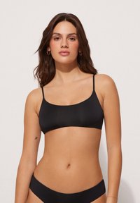 Černý bikiny top s tenkými ramínky, hladkým povrchem a minimalistickým designem. Obsahuje obdélníkový tvar a bezšvovou konstrukci.