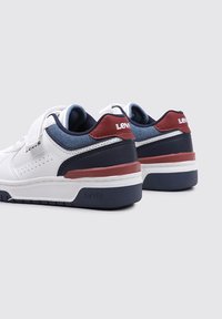 Zapatillas blancas con acentos en azul marino y rojo, presentan una superficie texturizada, detalles perforados y una correa de Velcro, con el logo de Levi's.