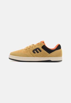 Zamszowe sneakersy w beżowym kolorze z czarnymi i pomarańczowymi akcentami. Posiadają perforowane detale, okrągły czubek oraz wyściełaną podeszwę. Klasyczny projekt na sznurówki.