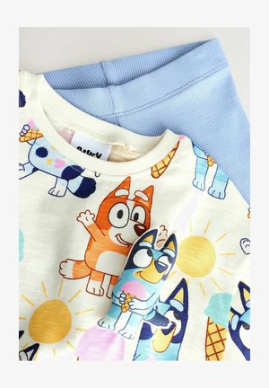 Leggings acanalados de color azul claro combinados con una camiseta crema con patrones de perros de dibujos animados coloridos, un sol y helados.