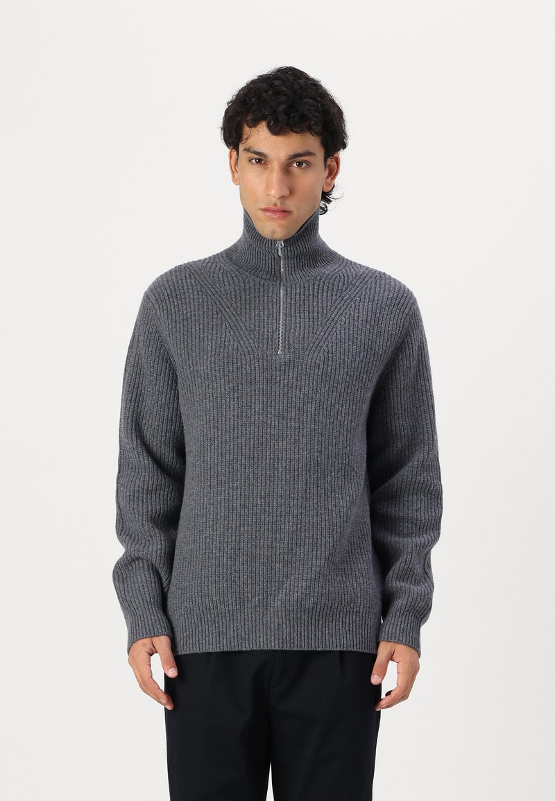 Grauer gerippter Pullover mit hohem Kragen und kurzem Reißverschluss. Strukturiertes Strickmaterial und lange Ärmel. Symmetrisches Design auf der Brust.