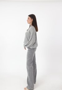 Grijze gebreide trui met verlaagde schouders, gecombineerd met lichtgrijze wijde pantalon. Beide kledingstukken hebben een zachte textuur.