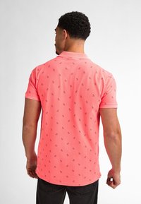 T-shirt med kort ärm i klar korall, med ett subtilt mönster av små, mörka symboler. Klassisk krage och design med regular fit.