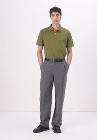 Olivgrön polo med orange krage, ihopparad med grå rutiga byxor. Svart bälte och skor fulländar outfiten. Slim-fit design.