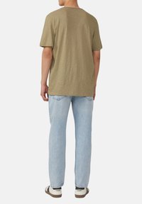 Olijfgroene T-shirt met korte mouwen, relaxte pasvorm, gecombineerd met lichtblauwe rechte jeans en beige sneakers met zwarte accenten.
