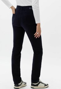 Marineblauwe corduroypantalons met een slim fit ontwerp, achterzakken en een subtiele textuur, gecombineerd met zwart-witte sneakers.