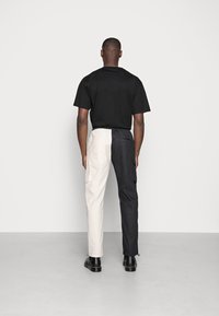 Musta lyhythihainen paita yhdistettynä värilohkottuihin housuihin, joissa puolet on beigeä ja puolet mustaa, sivutaskuilla ja kapenevalla istuvuudella.