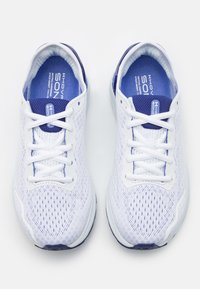 Witte sportieve schoenen met een ademend bovenwerk van mesh, blauwe accenten op de zolen en hak, en platte veters. Ontworpen voor comfort en ondersteuning.