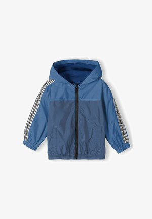 Veste coupe-vent bleu clair avec capuche, fermeture éclair à l'avant, poignets élastiques et accents de rayures blanches sur les manches. Fabriquée en matériau lisse et léger.