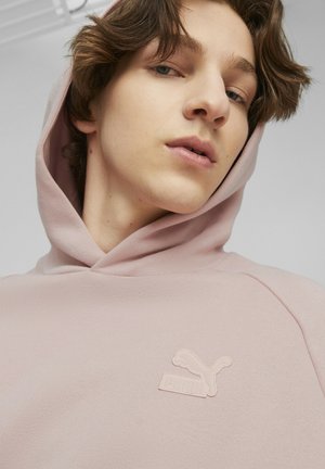 Haut à capuche rose avec cordon de serrage et logo Puma brodé sur la poitrine. Texture lisse avec une coupe décontractée et un design minimaliste.
