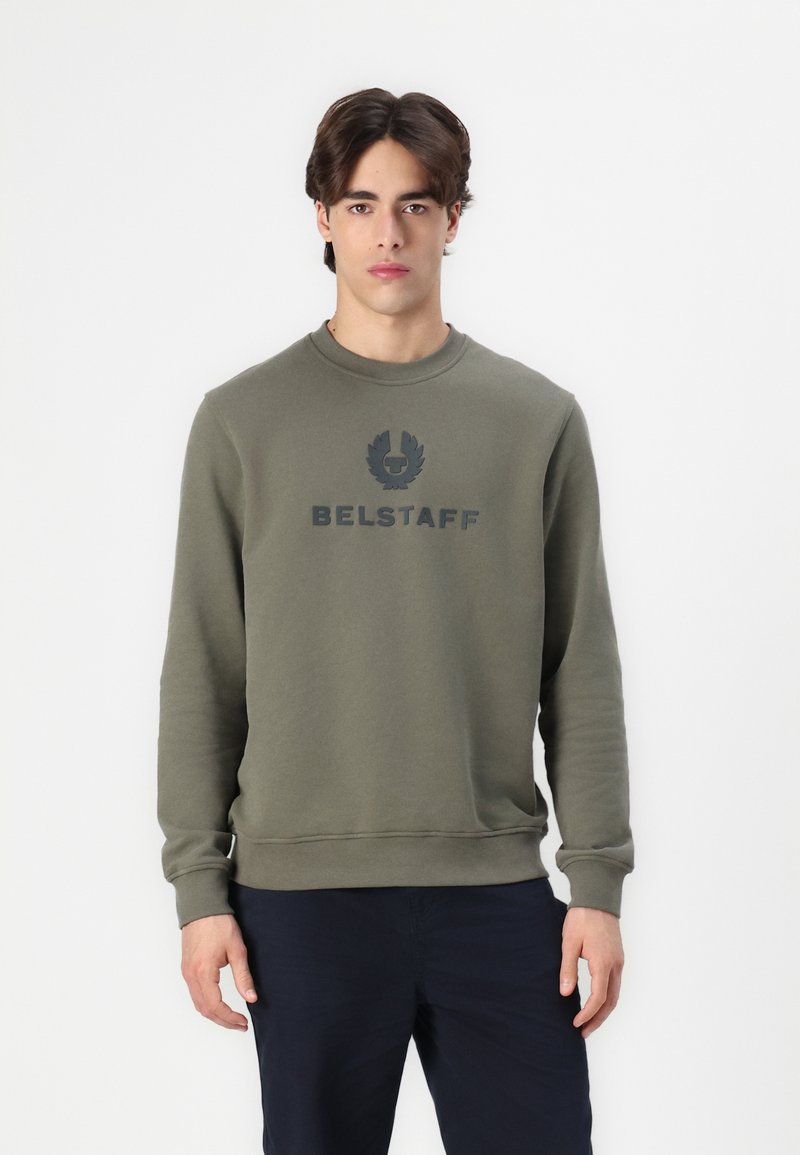 Maslinasto zelena dukserica s okruglim izrezom i rebrastim manžetama. Ispisani "BELSTAFF" logo u tamno sivoj boji preko prsnog dijela. Glatka tekstura.