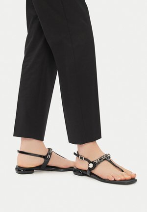 Sandali in pelle verniciata nera con design a infradito, caratterizzati da un accento a catena e una piccola fibbia sul cinturino alla caviglia. Suola piatta.