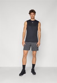 Sort ærmeløs træningstop, grå shorts, sorte løbesko og sorte sokker. Glat stof, tætsiddende design og minimal branding.