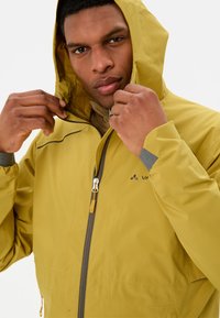 Veste imperméable jaune avec capuche, présentant une fermeture éclair, des accents gris et une doublure intérieure à motifs.