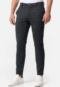 Pantalones de cuadros grises confeccionados en tejido entrelazado, con un ajuste slim, frente plano y cierre de botón, combinados con zapatillas blancas.