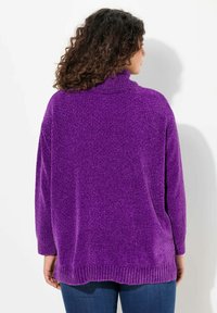 Lila, texturerad tröja med hög krage, sänkt axel och ribbad nederkant. Materialet verkar mjukt och mysigt, lämpligt för avslappnad klädsel.