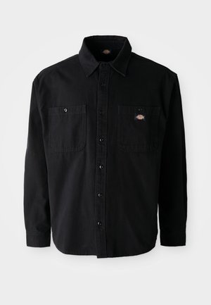 Black long-sleeve button-up shirt with two chest pockets and a logo patch. Made of a sturdy fabric with a smooth texture and classic collar.