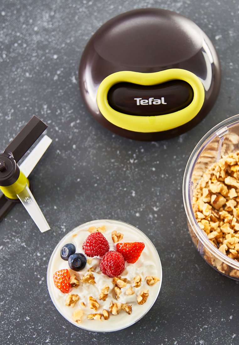 Yaourtière Tefal marron avec un accent jaune. Le bol contient du yaourt garni de granola, de framboises, de myrtilles et de fraises.