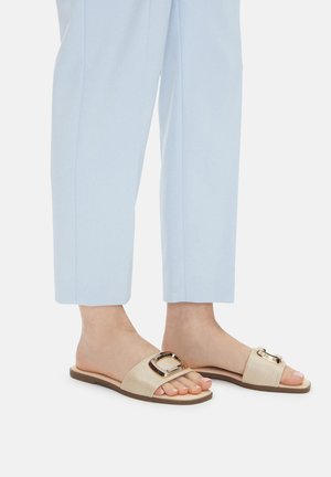 Beżowe sandały na płaskiej podeszwie z fakturowaną cholewką, ozdobione wyraźnym metalowym klamrą, zestawione z jasnoniebieskimi, dopasowanymi spodniami.