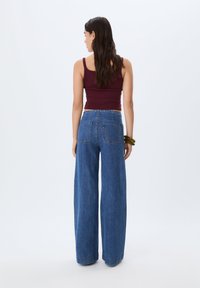 Top corto borgogna abbinato a jeans in denim blu a vita alta e gamba larga. I jeans presentano due tasche posteriori, vestibilità strutturata e orlo leggermente sfilacciato.