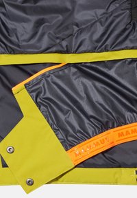 Leichtgewichtige grüne und schwarze Jacke mit Innenfutter, das einen orangefarbenen Reißverschluss und ein Logo aufweist. Glattes, wasserabweisendes Material; enthält Kontrastbesatz.