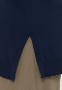 Ναυτικό πλέ knit πουλόβερ με ραμμένο στρίφωμα και πλευρικές σχισμές, επικαλυμμένο με χακί ύφασμα. Μαλακή υφή και ευθεία σιλουέτα με ελάχιστες λεπτομέρειες.