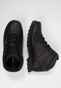 Botas de senderismo de cuero negro con puntera redonda, cuello acolchado, suela de goma resistente y sistema de cordones. Diseño minimalista con logo en relieve en la lengüeta.