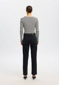 Fekete-fehér csíkos hosszú ujjú felső, magasderekú fekete farmernadrággal párosítva. Vékony szabású, enyhén szűkülő szárú nadrág, melyen hátul zsebek láthatók.