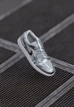 Zilveren sportieve schoen met een glanzende afwerking, gaaspanelen en gestructureerde accenten. Voorzien van een vetersluiting en een rubberen zool.