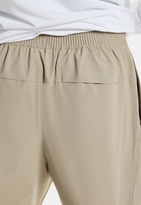 Jasnobeżowe szorty z elastycznym paskiem, charakteryzujące się gładką fakturą i brakiem widocznych wzorów czy akcentów. Zbliżenie na tylny widok.