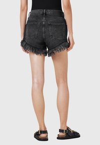 Shorts in denim nero con orli sfrangiati, due tasche posteriori e cintura cucita. Abbinati a sandali neri con un accento dorato.